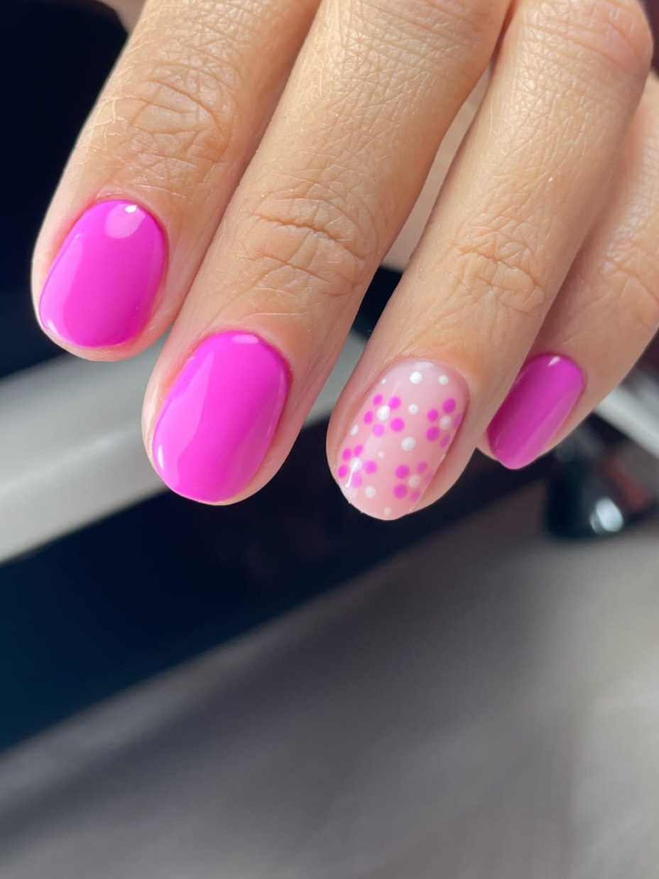 Korte fuchsia gelnagels met één nude accentnagel met roze stippen