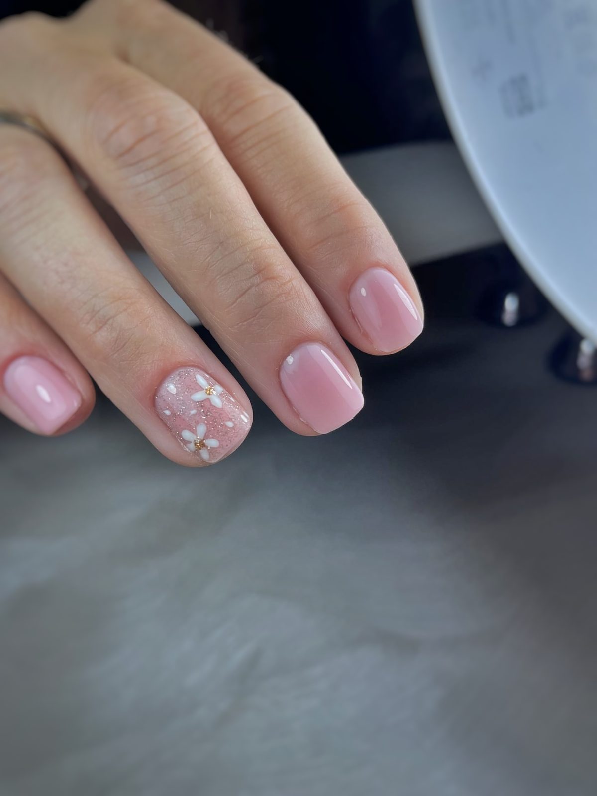 Korte zachtroze nagels met een wit bloemetje op de ringvinger