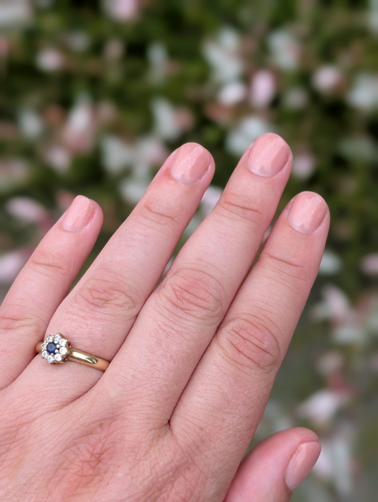 Zachtroze korte nagels met een ring, voor bloeiende struiken