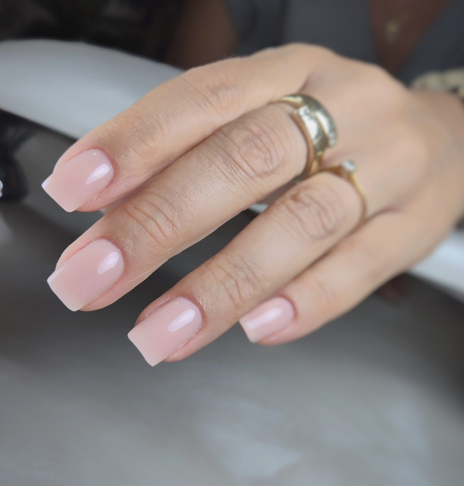 Doorschijnend roze square nagels met gouden ringen, op de nageltafel